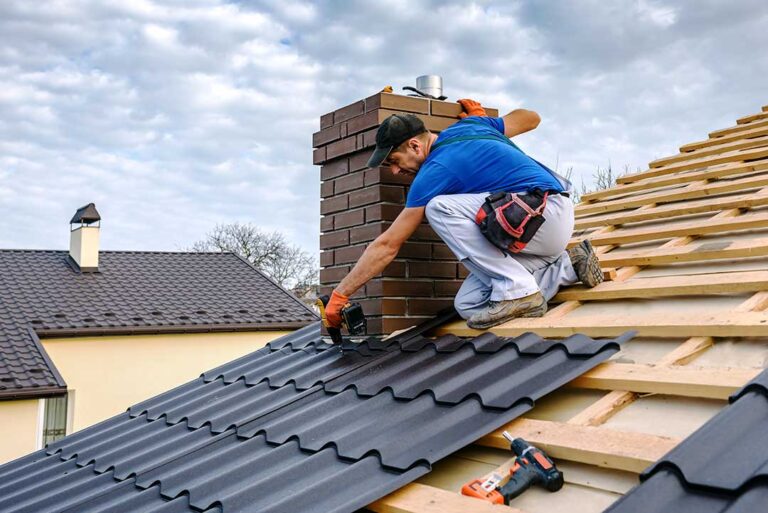 A homeowner on a sturdy ladder removes leaves and debris from a residential gutter.